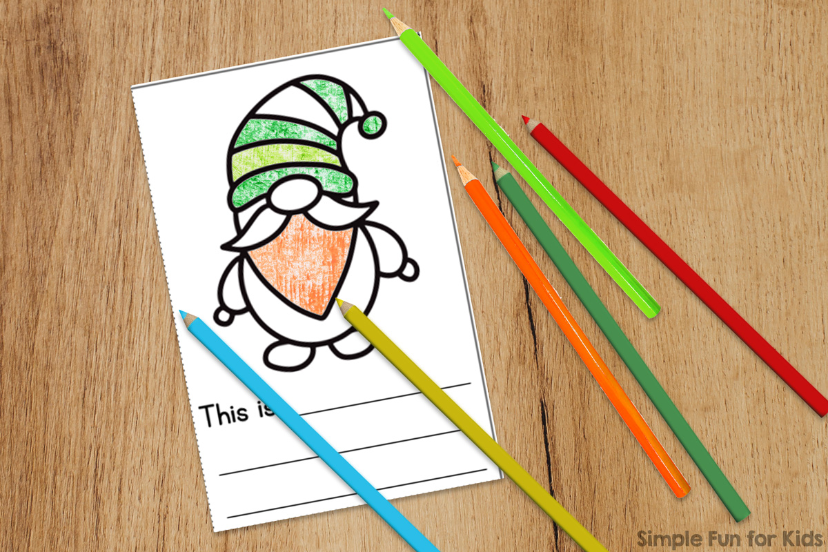 Picture of one page of the writing-prompts version of the Gnome Mini Folding Coloring Books on top of a light brown desktop with colored pencils on top. Part of the gnome is colored in in orange, light green, and dark green.