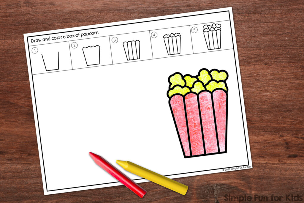 Picture of one of the four different versions of the popcorn directed drawing worksheets. The popcorn box is colored in with red and yellow crayons that lay on top of the paper. The paper and crayons are on top of a dark brown wooden tabletop.