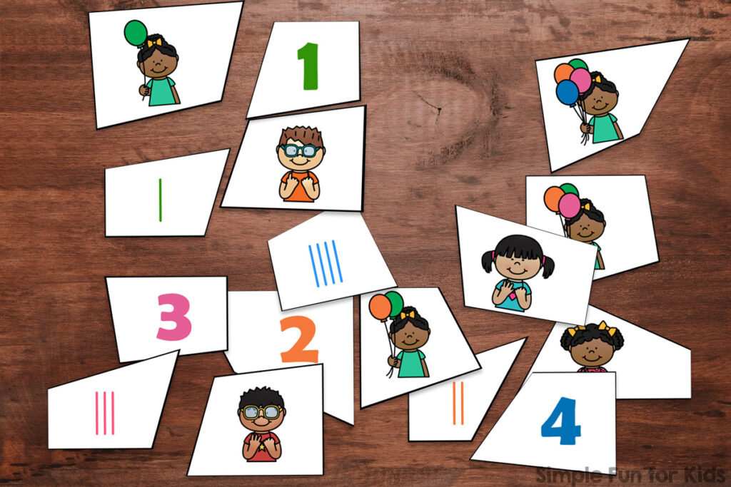 Puzzle pieces for numbers 1-4 of the printable 4-piece balloon counting puzzles on top of a dark brown table top. Each puzzle consists of the numeral, tally marks, an image of a kid holding that number of balloons, and a kid holding up that many fingers.