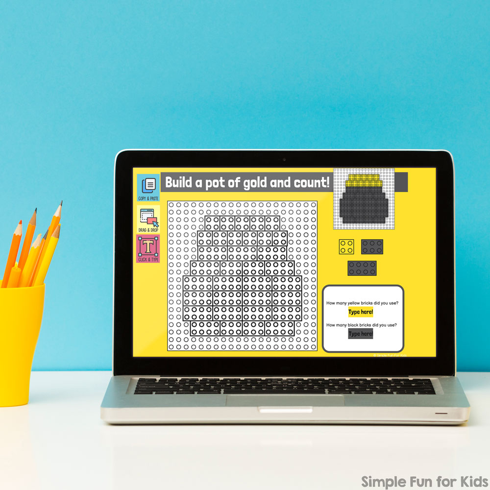 Picture of a laptop in front of a blue wall with a yellow cup and yellow pencils next to it. The laptop screen shows a pot of gold to be built from digital building bricks.