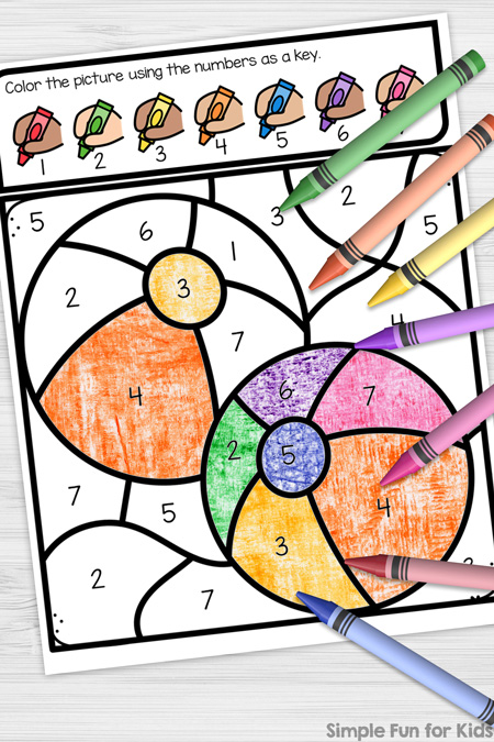 Picture of the Beach Ball Color by Number Coloring Page on top of a white desk. The image is partially colored in and crayons in 7 colors are scattered on top of the paper. There's a Simple Fun for Kids watermark in the bottom right corner.